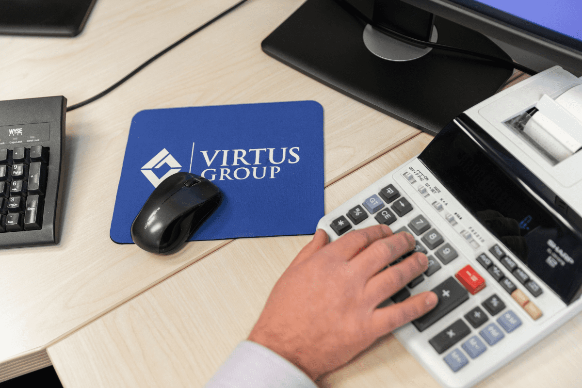 Person at desk with calculator and blue Virtus Group mousepad